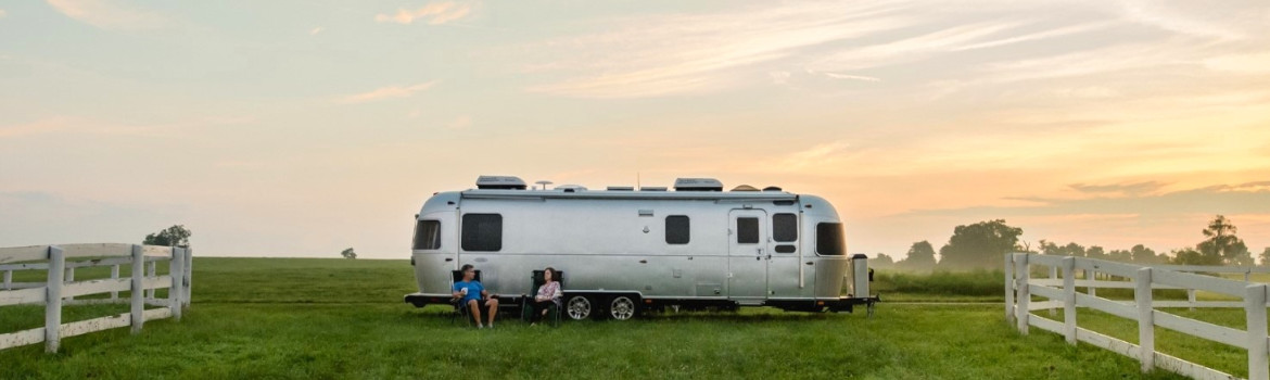 Two people sitting and relaxing in front of an Airstream® RV parked outside on a property