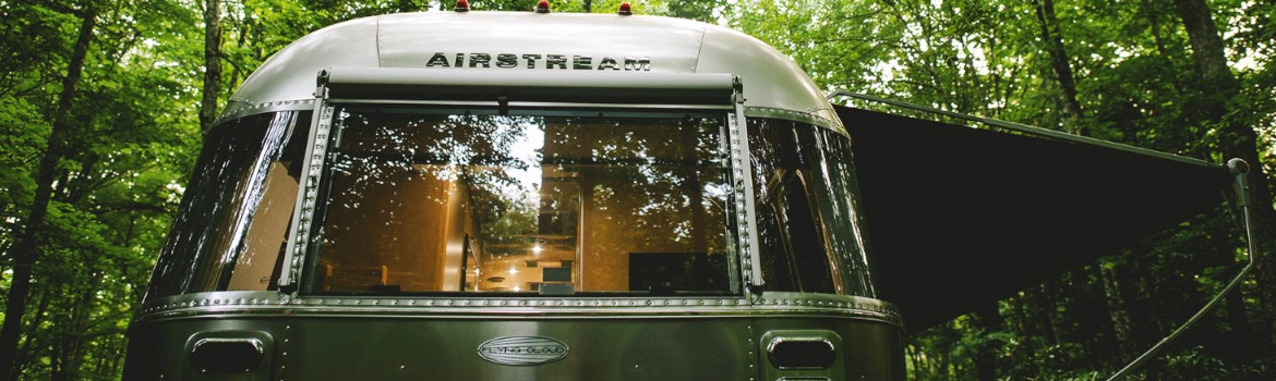 Airstream® trailer parked in a forest with interior lights on and open awning